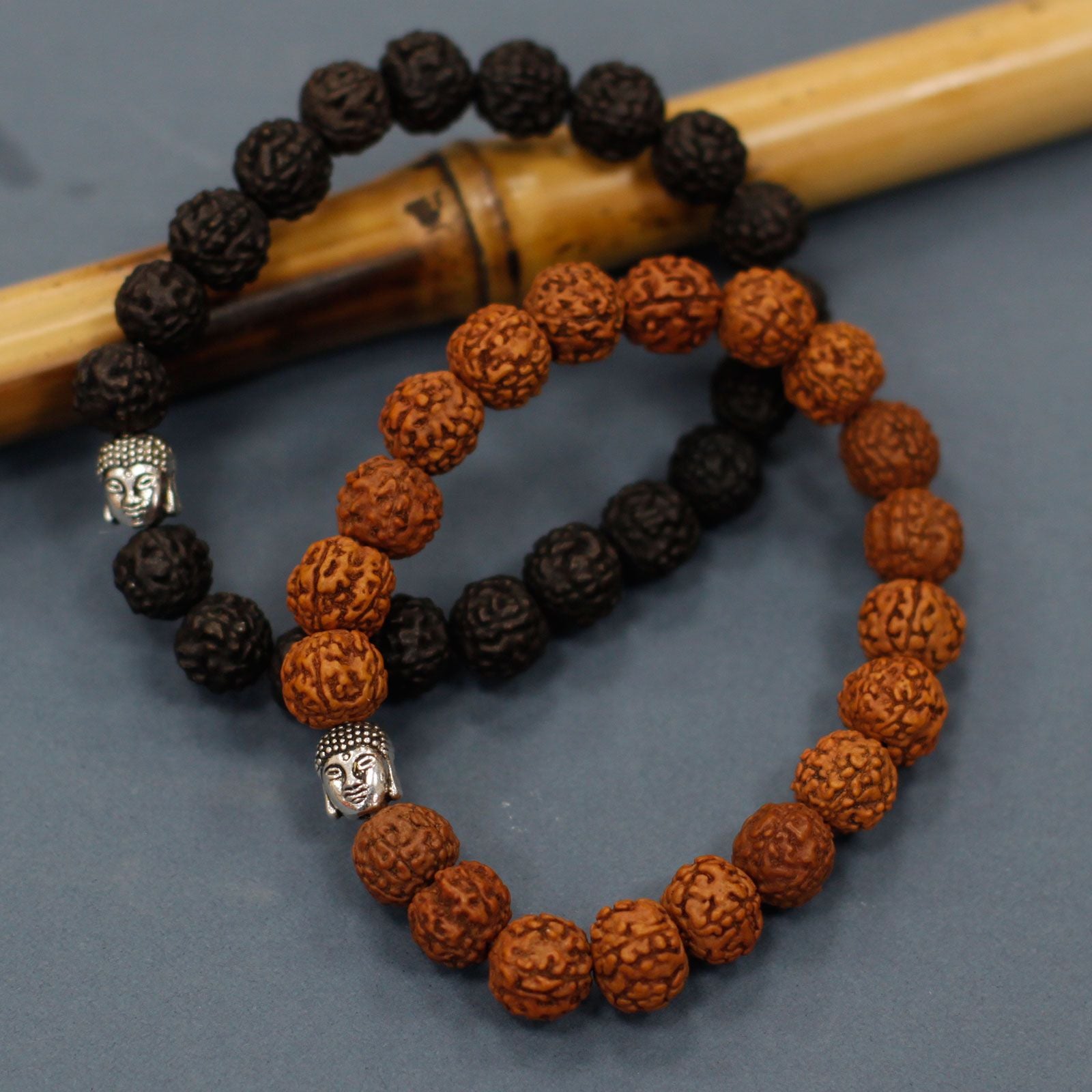 Bracelets en perles rudraksha noir et brun avec tête de Bouddha disposés autour d’un bâton dans une ambiance zen