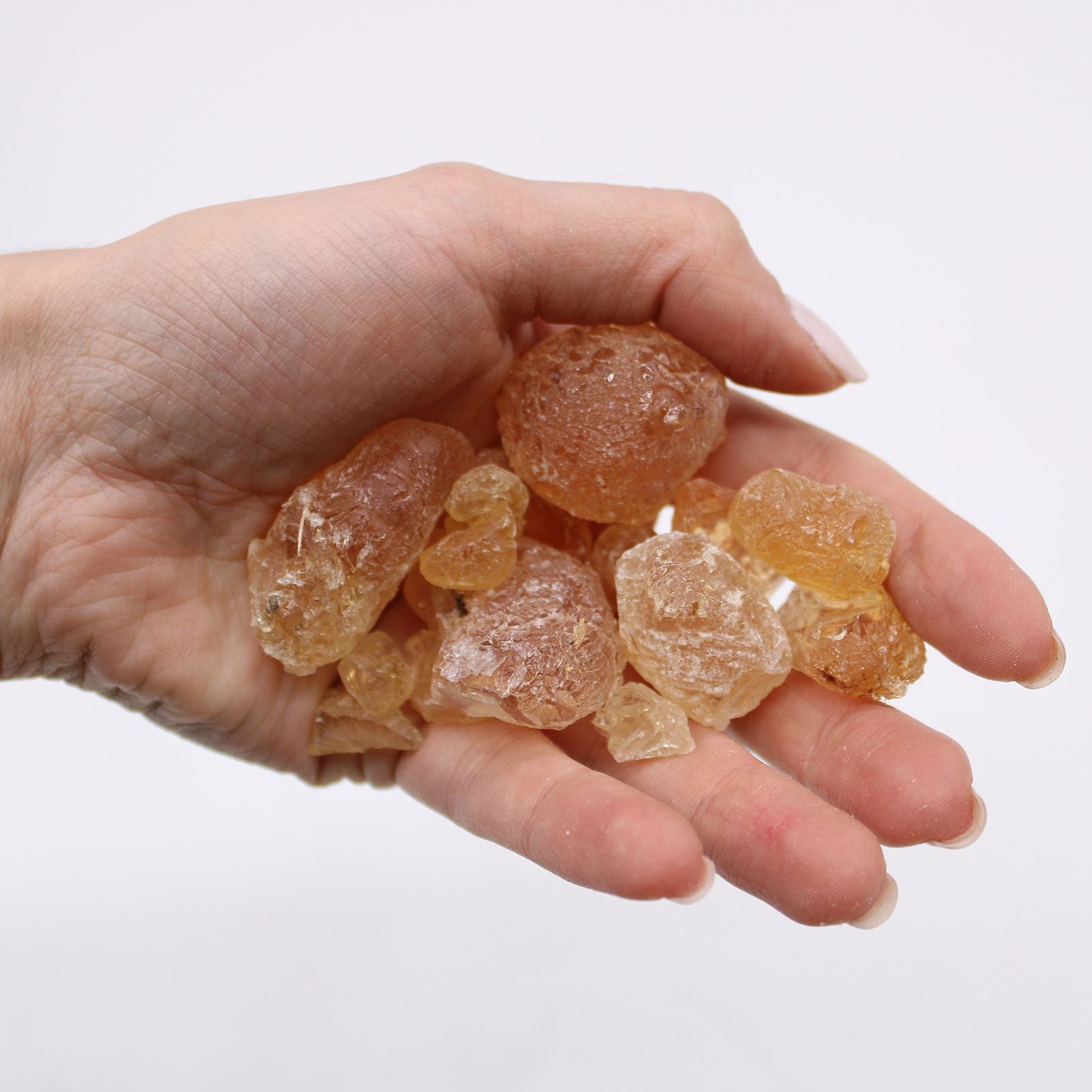 Morceaux translucides de résine de gomme arabique aux reflets ambrés en gros plan, accompagnés d’une main tenant quelques fragments pour montrer la texture légère et cristalline