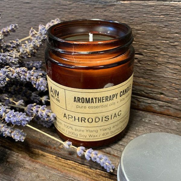 Bougie aromathérapie Aphrodisiaque à base d’huile essentielle d'ylang ylang et patchouli, posée sur une surface en bois avec des brins de lavande, ambiance naturelle et relaxante