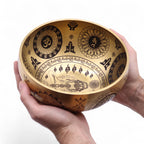 Bol chantant tibétain en laiton gravé tenu dans une main montrant sa taille compacte et ses détails spirituels