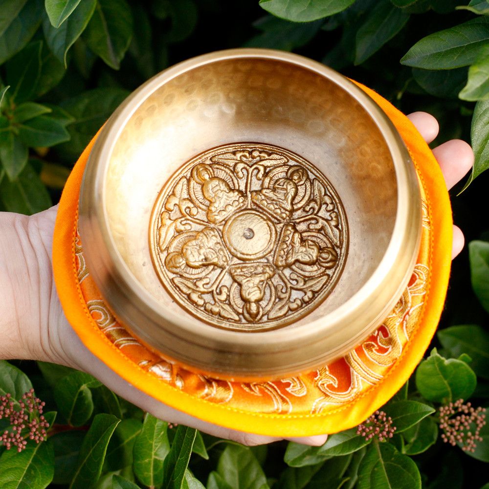 Bol chantant tibétain 5 bouddha posé sur coussin orange dans un décor naturel pour méditation et détente