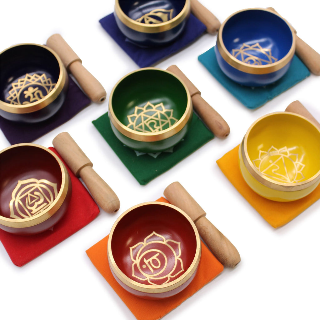 Ensemble de 7 bols chantants chakras posés sur coussins colorés avec maillets, représentant les centres énergétiques du corps