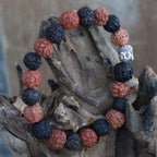 Bracelet rudraksha avec tête de Bouddha mix noir et marron posé sur morceau de bois