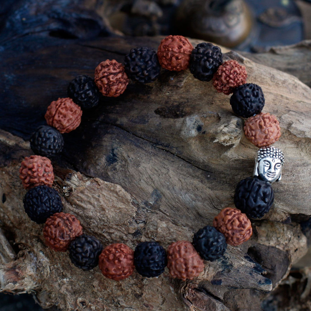 Bracelet en perles rudraksha mix noir et marron avec tête de Bouddha posé sur bois ambiance méditation