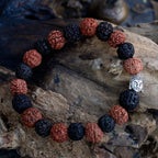 Bracelet en perles rudraksha mix noir et marron avec tête de Bouddha posé sur bois ambiance méditation