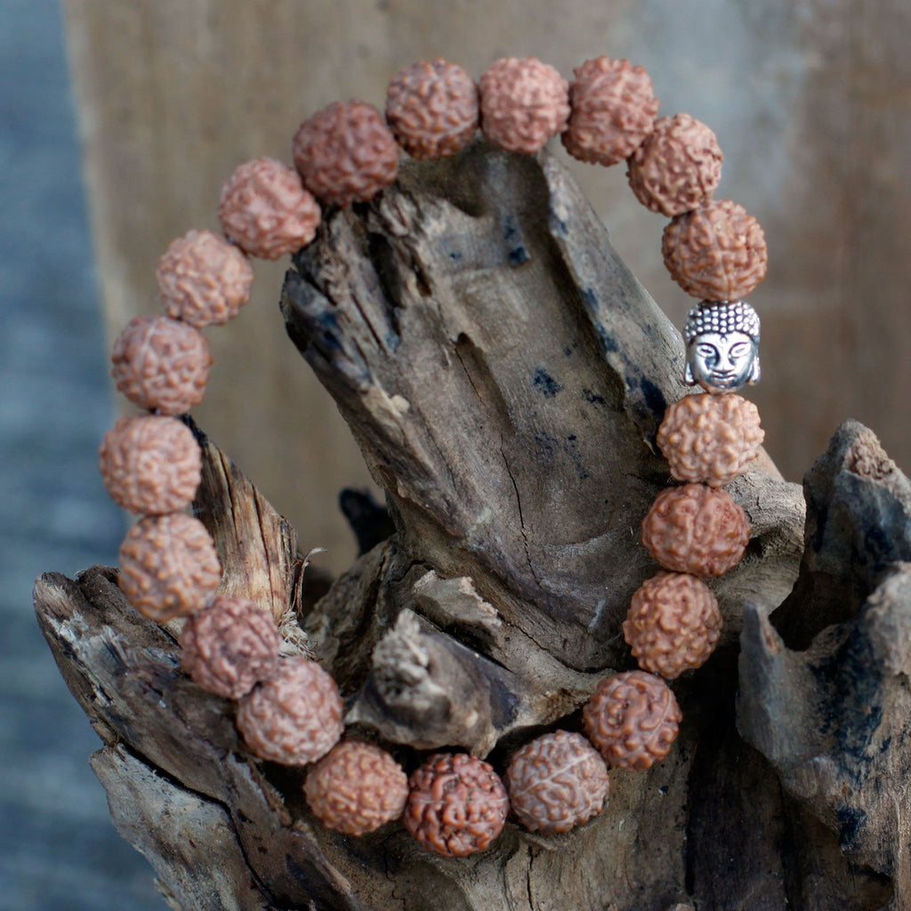Bracelet en perles rudraksha marron avec tête de Bouddha posé sur bois ambiance méditation