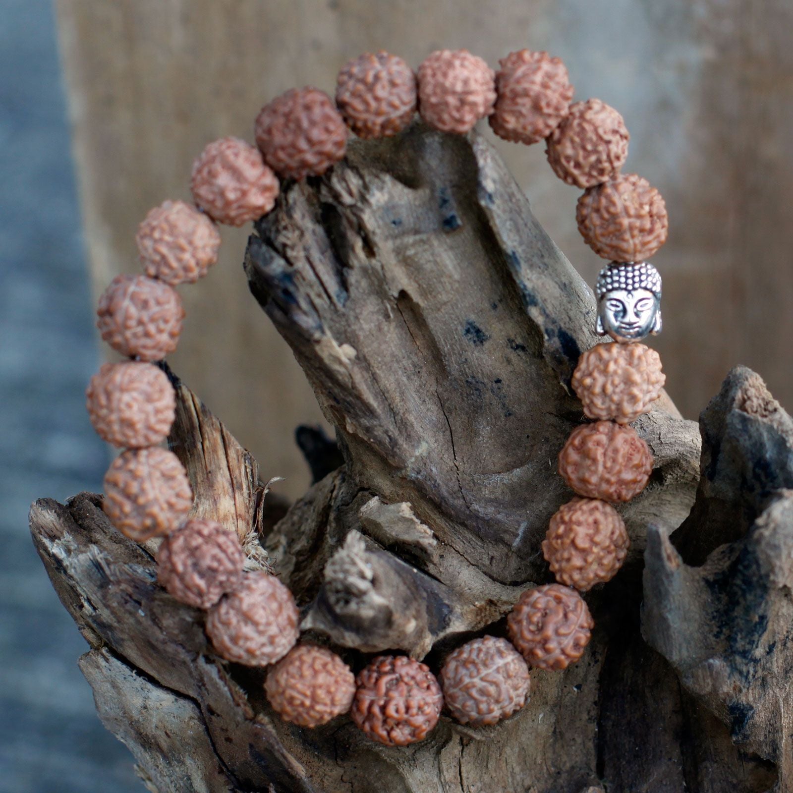 Bracelet en perles rudraksha marron avec tête de Bouddha posé sur bois ambiance méditation
