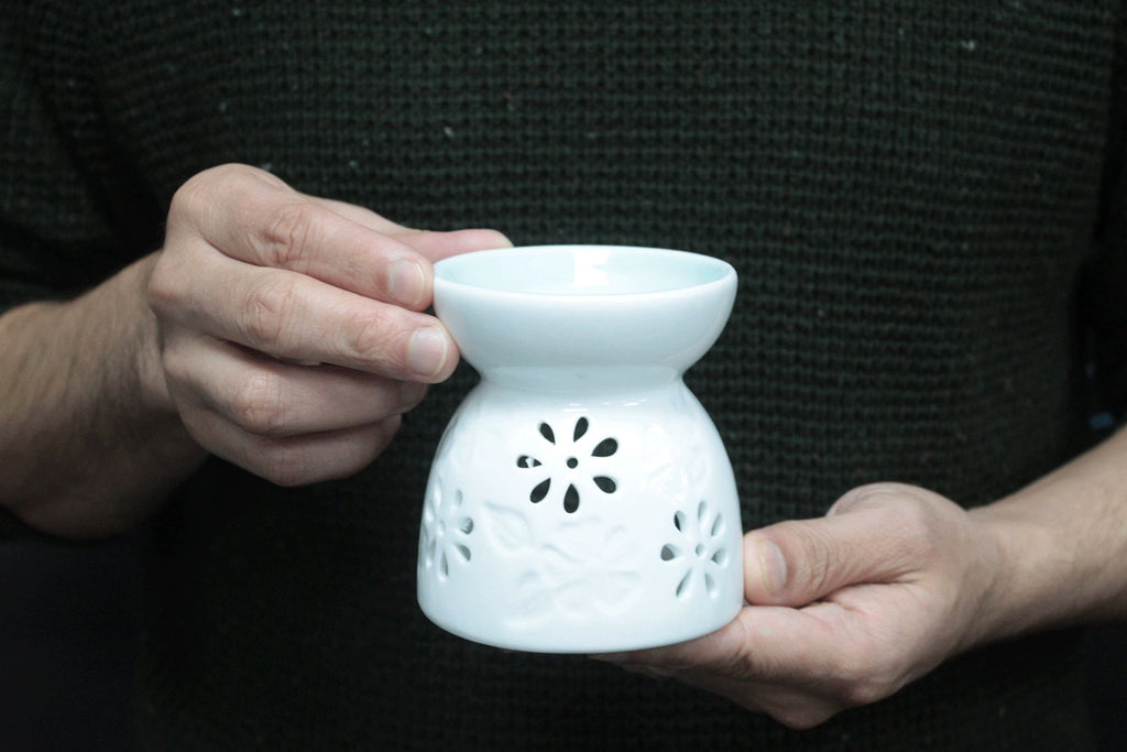 personne tenant un brûleur à huile en céramique blanche utilisé pour diffusion de parfum et ambiance zen