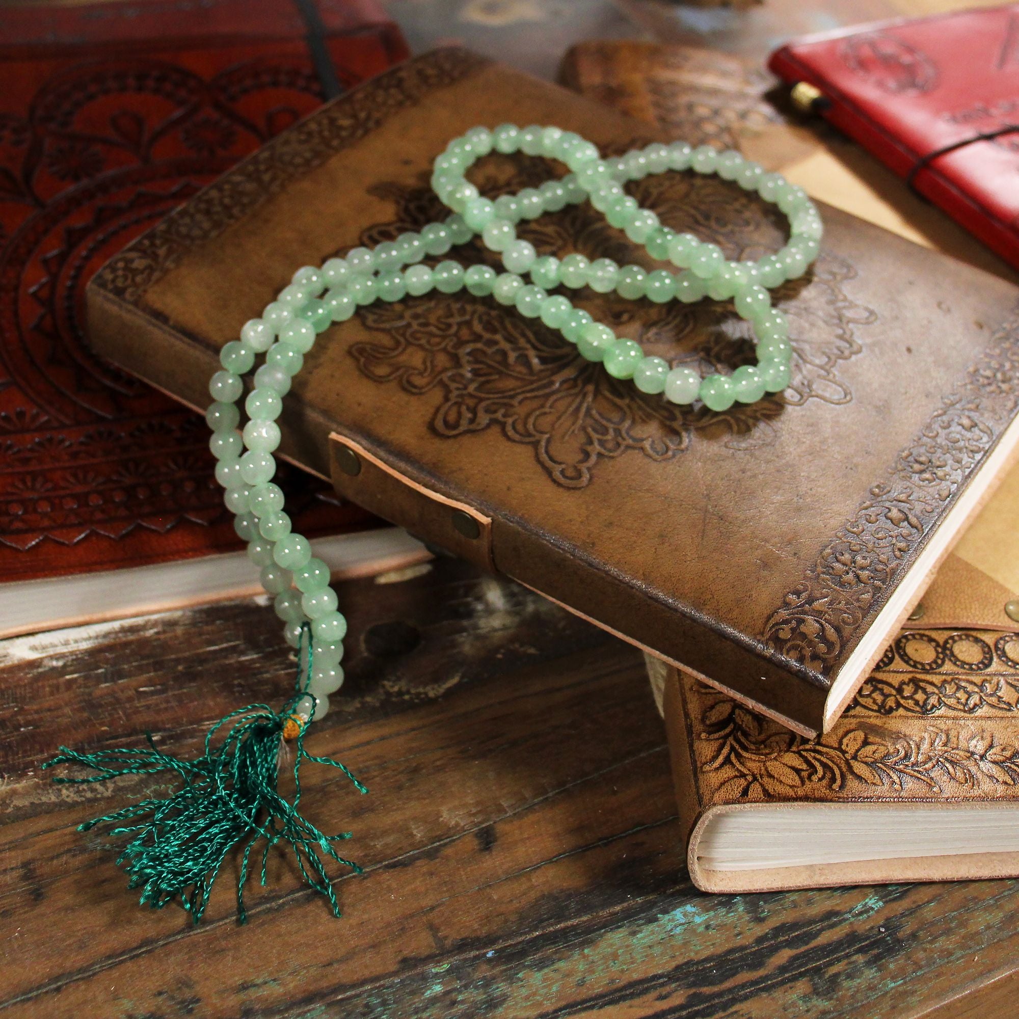 Collier mala 108 perles en pierre naturelle aventurine avec pompon vert, disposé sur livre prière sur table en bois, bijou spirituel pour meditation chakra et bien etre