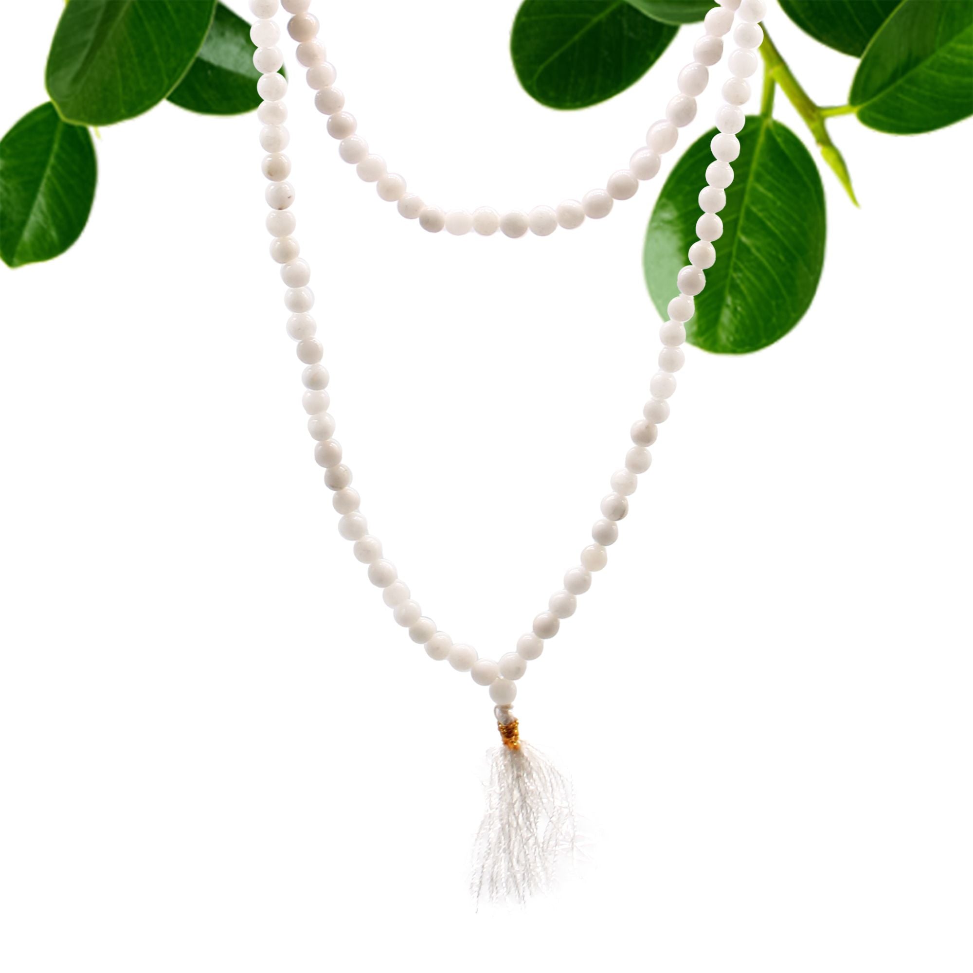 Collier mala 108 perles en pierre naturelle quartz blanc avec pompon blanc, suspendu avec feuilles vertes en arriere plan, bijou spirituel pour meditation chakra et bien etre