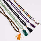 Plusieurs malas en pierres naturelles alignes sur fond clair avec pompons colores, comprenant oeil de tigre, aventurine verte, agate noire, amethyste et mala 9 planete astro