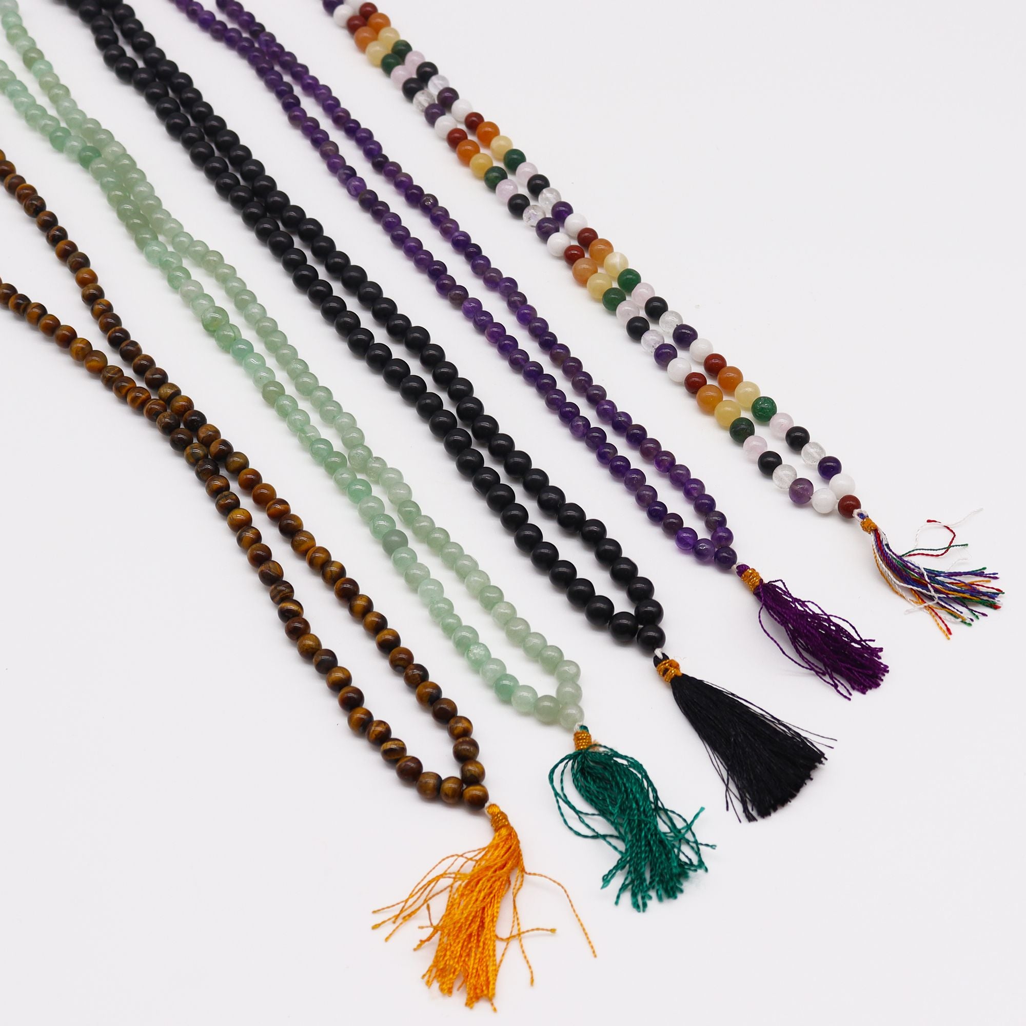 Plusieurs malas en pierres naturelles alignes sur fond clair avec pompons colores, comprenant oeil de tigre, aventurine verte, agate noire, amethyste et mala 9 planete astro