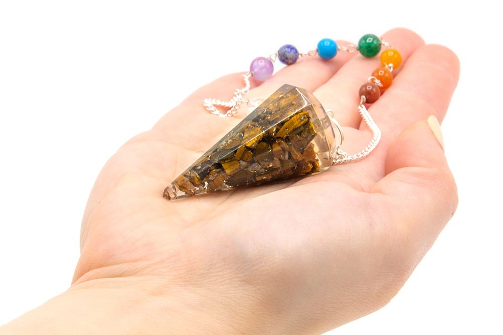 Pendule orgonite oeil de tigre tenu en main pour radiesthésie, divination et travail énergétique
