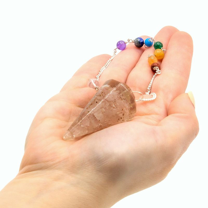 Pendule orgonite quartz rose tenu en main pour radiesthésie, divination et travail énergétique