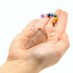 Pendule orgonite quartz rose tenu en main pour radiesthésie, divination et travail énergétique