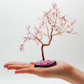 Arbre en quartz rose posé dans une main avec base rose et pierres délicates symbolisant amour et douceur