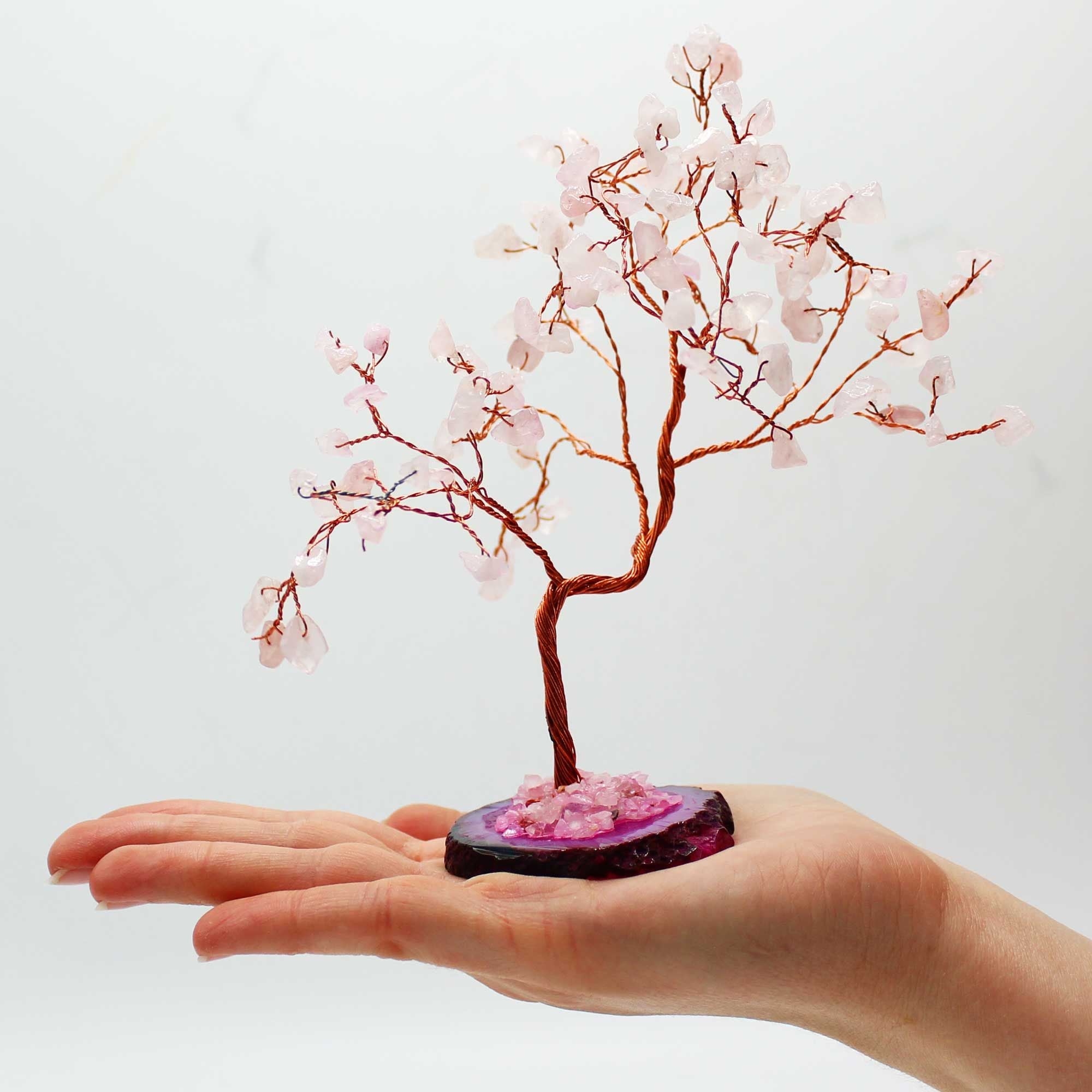 Arbre en quartz rose posé dans une main avec base rose et pierres délicates symbolisant amour et douceur