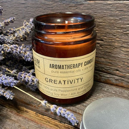 Bougie aromathérapie Créativité à base d’huile essentielle de menthe poivrée et clou de girofle posée sur une surface en bois avec des brins de lavande, ambiance naturelle et relaxante
