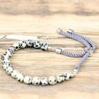 Bracelet en pierre naturelle jaspe dalmatien ajustable avec cordon gris et perles noir et blanche posé sur table en bois