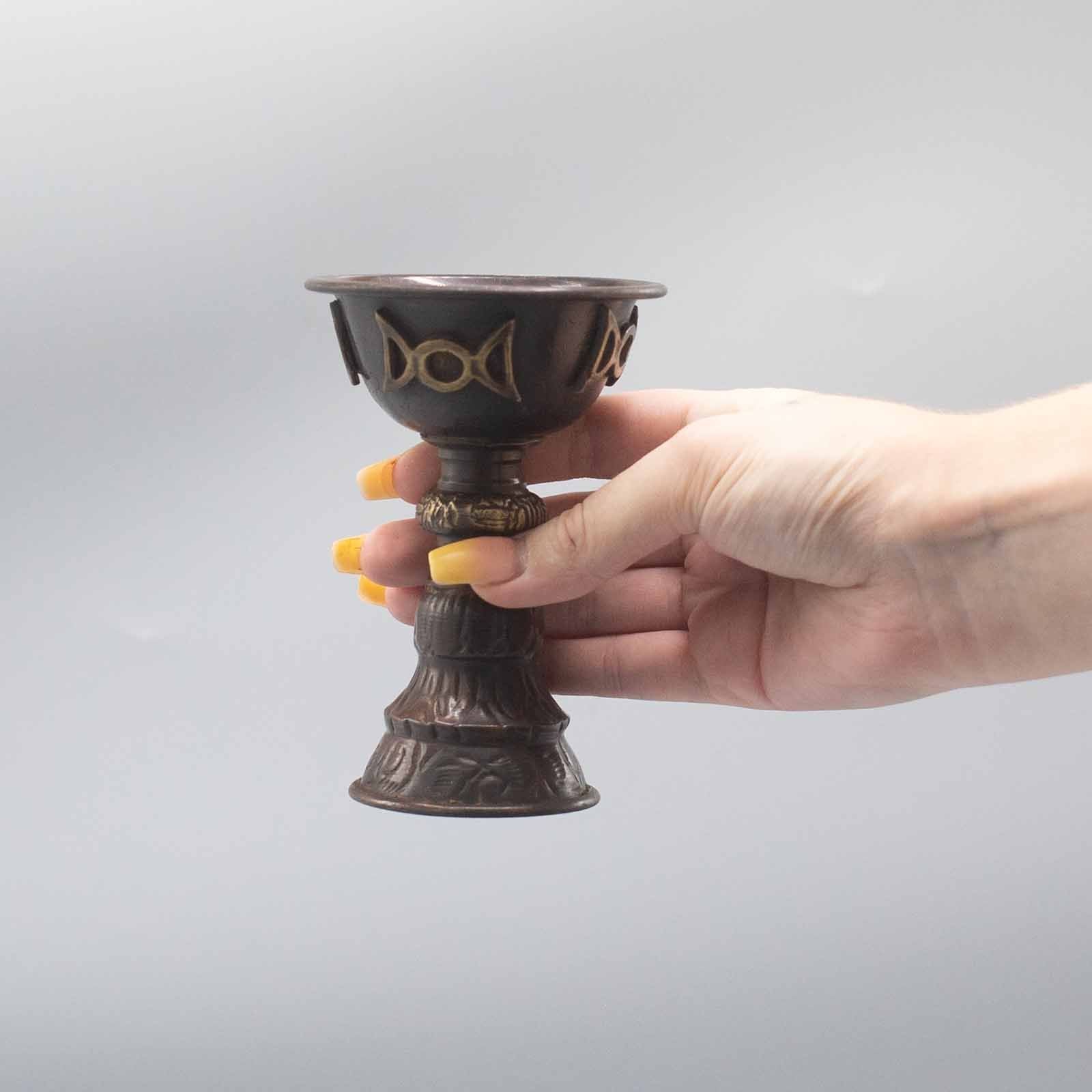 Calice rituel en cuivre tenu en main avec symbole triple lune, utilisé lors de cérémonies et rituels spirituels