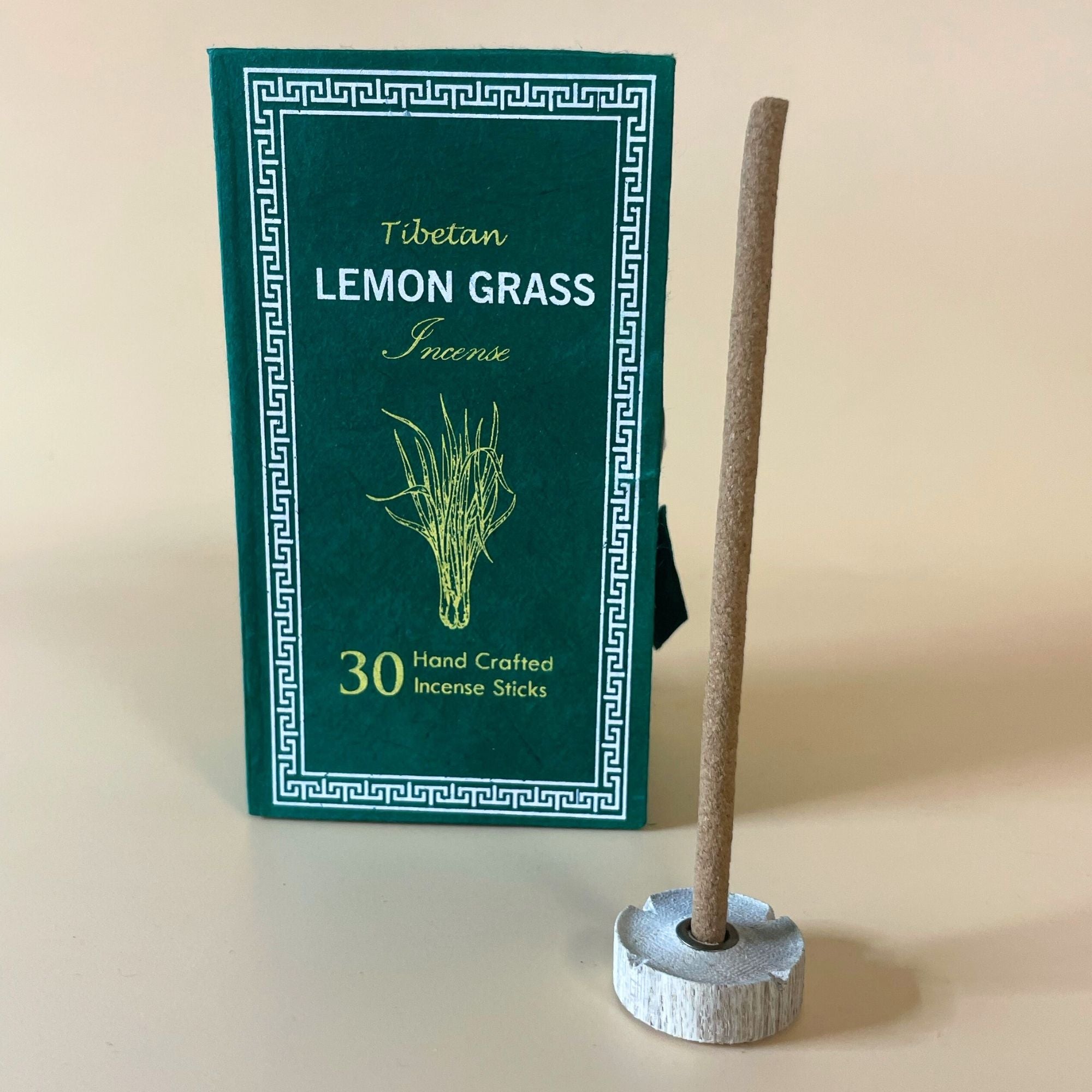 Encens tibétain citronnelle avec bâtonnet posé sur support et coffret vert en arrière-plan