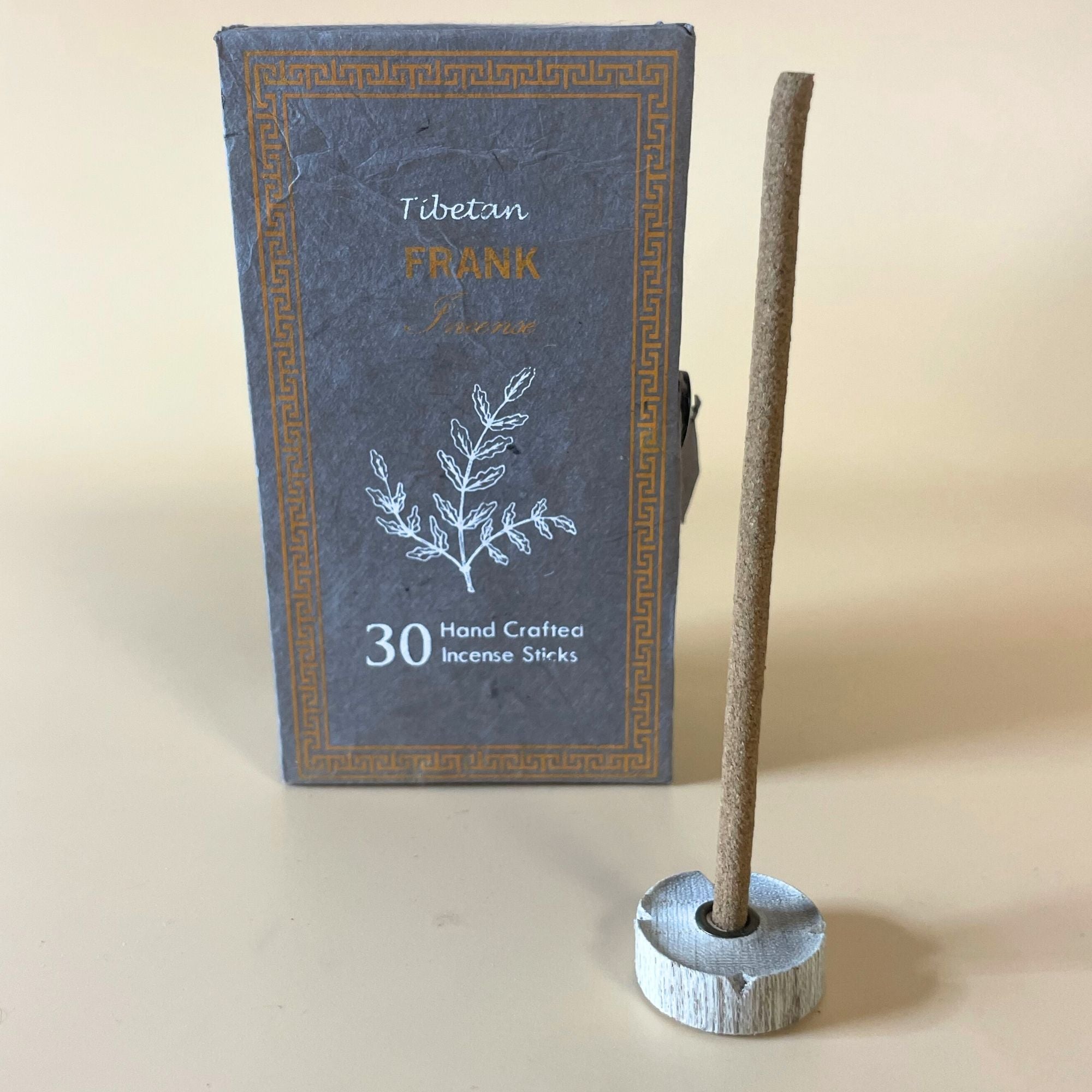 Encens tibétain oliban avec bâtonnet posé sur support et coffret vert en arrière-plan