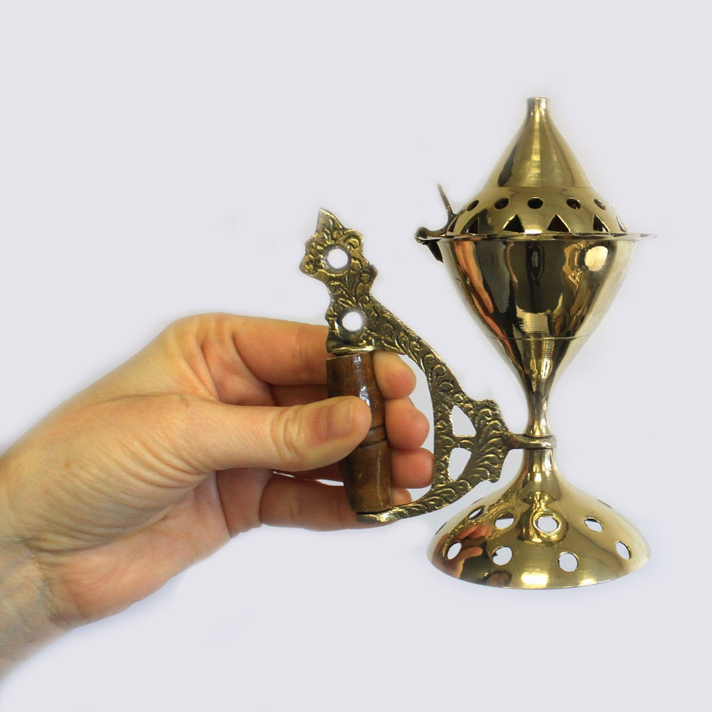 main tenant un grand brûleur d’encens en laiton avec manche bois montrant sa taille pour rituels et parfum d’intérieur