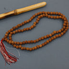 Mala en rudraksha posé à côté d’un accessoire en bois, avec pompon rouge et blanc, utilisé pour la méditation.