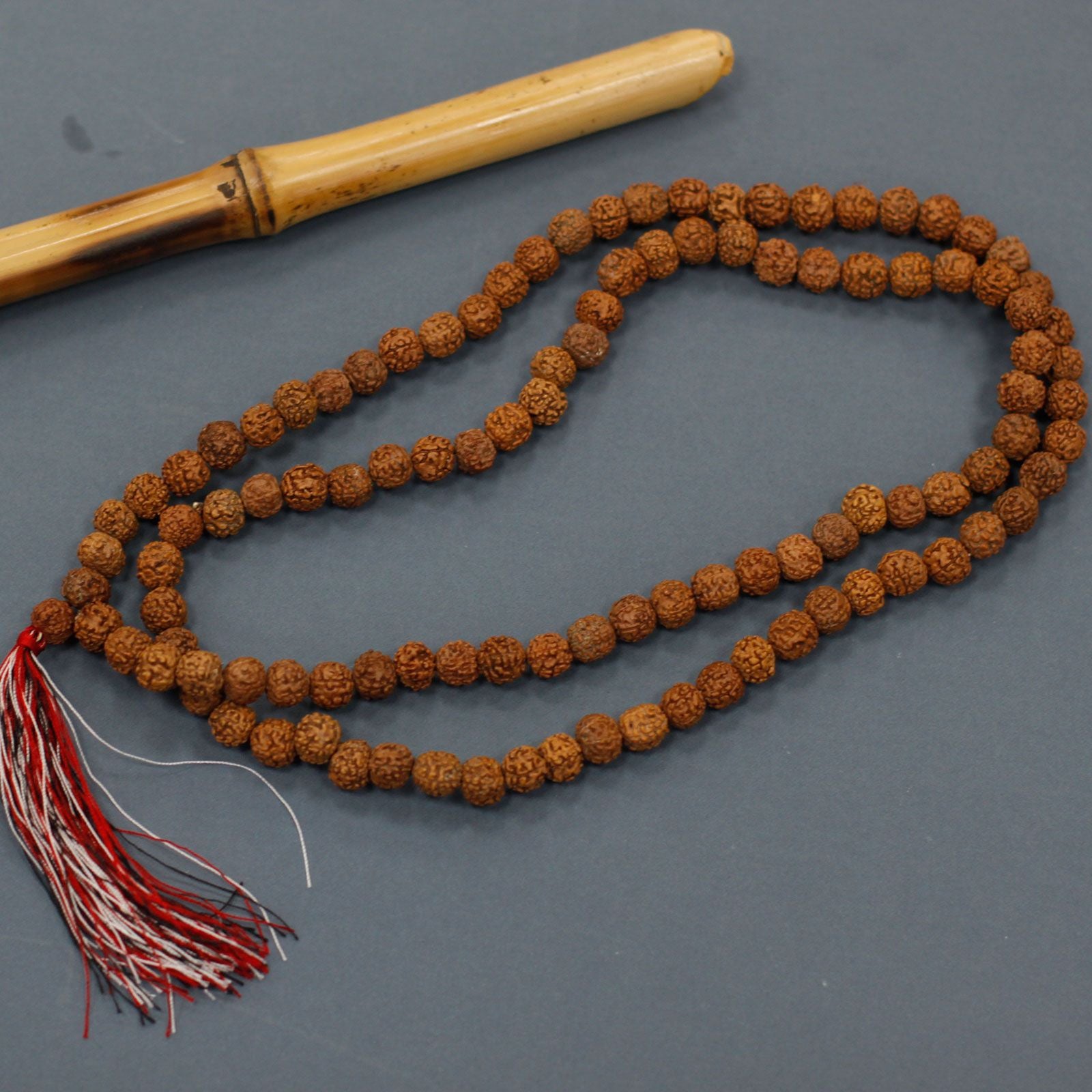 Mala en rudraksha posé à côté d’un accessoire en bois, avec pompon rouge et blanc, utilisé pour la méditation.