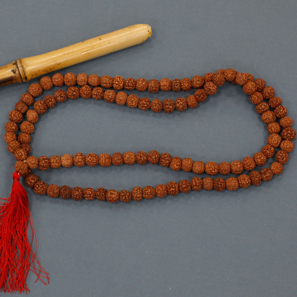 collier mala rudraksha comprenant un mala collier avec perles marron et pompon rouge, sur fond gris