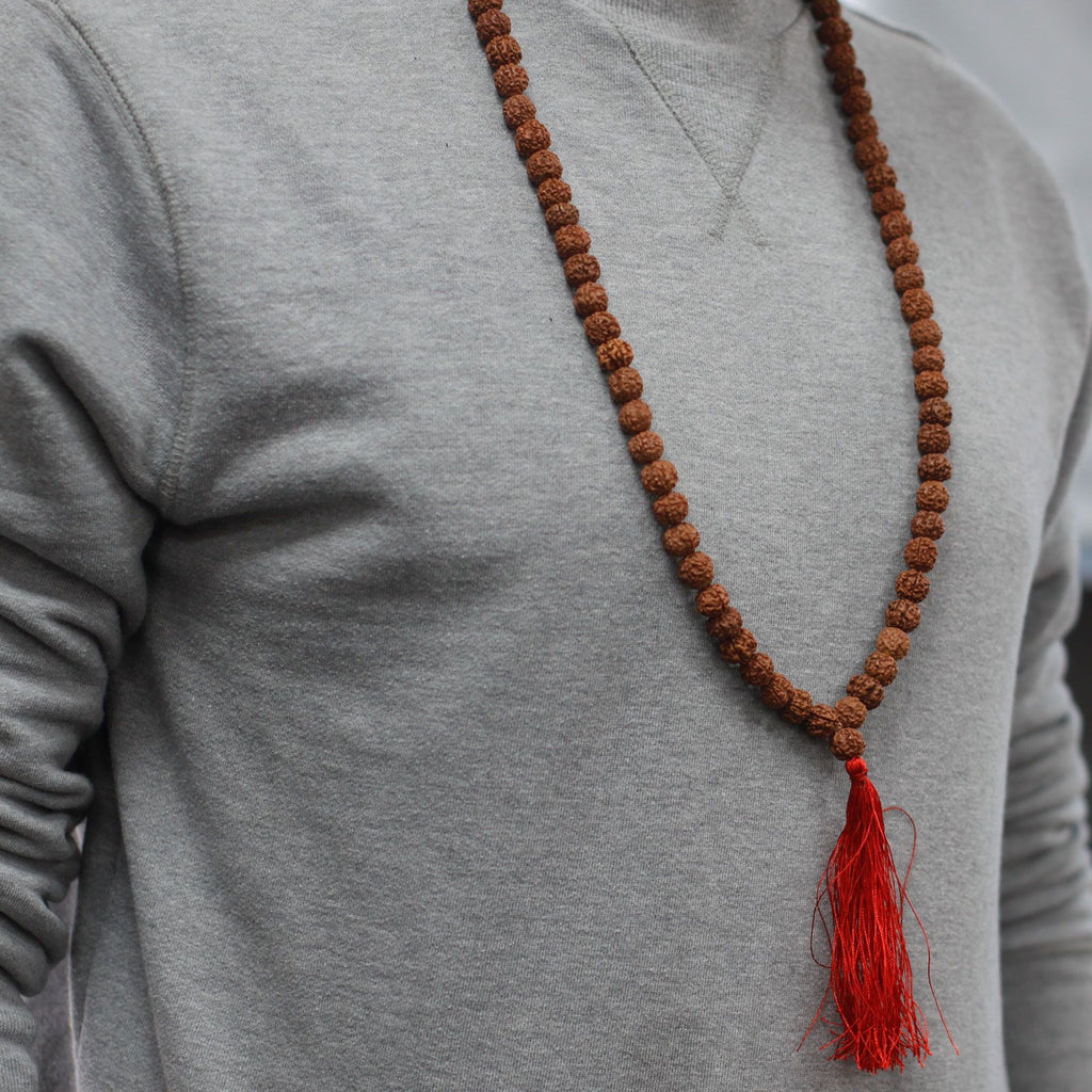 Personne portant un mala rudraksha en collier avec pompon rouge sur un vêtement clair, style minimaliste et naturel.