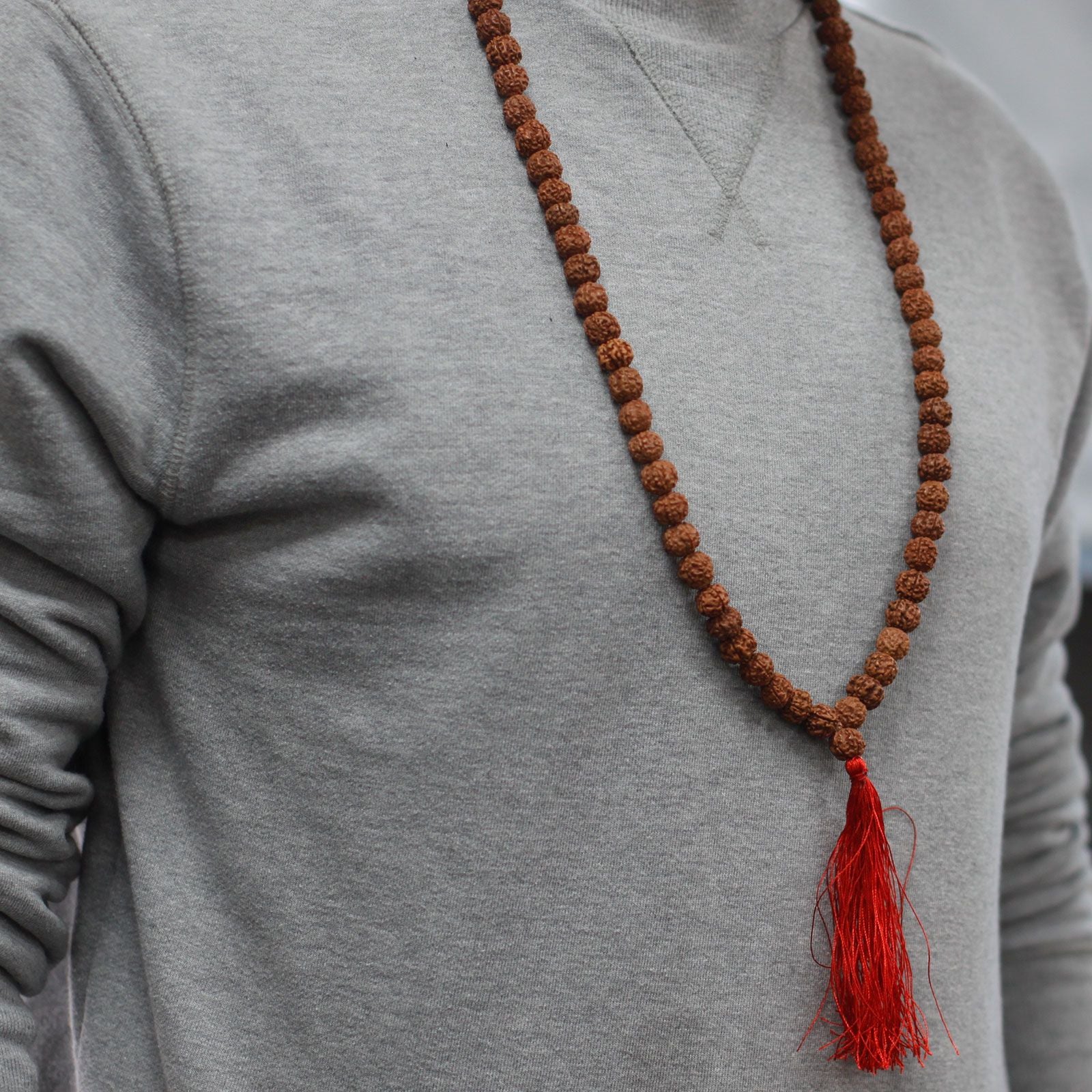 Personne portant un mala rudraksha en collier avec pompon rouge sur un vêtement clair, style minimaliste et naturel.