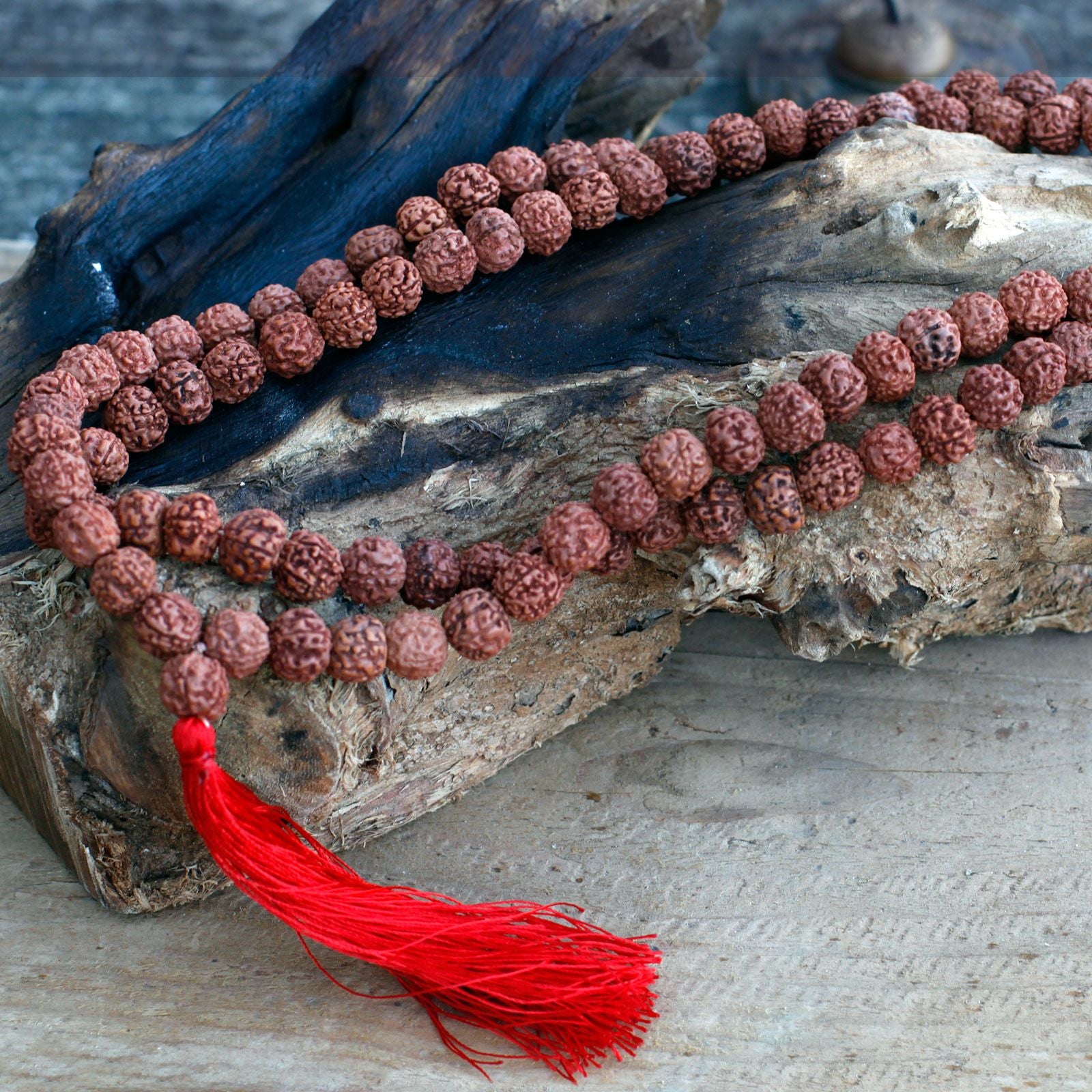Mala en perles de rudraksha marron posé sur une surface en bois brut avec pompon rouge et blanc, ambiance naturelle et authentique.