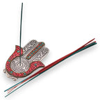 Porte-encens Hamsa rouge et vert avec bâton d’encens allumé, utilisé pour purification énergétique et rituel bien-être