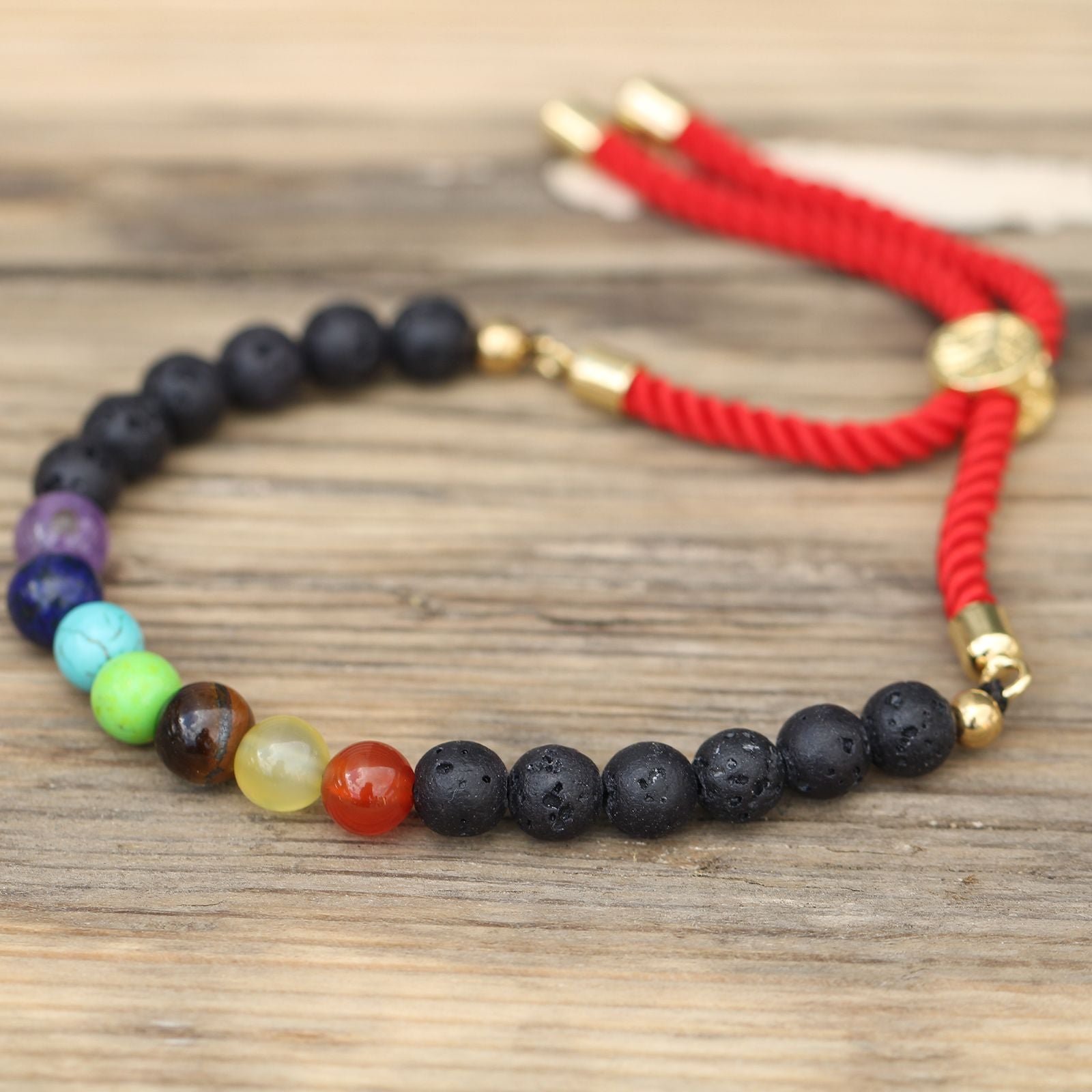 Bracelet en pierre de lave naturelle et 7 chakras ajustable avec cordon rouge et perles noir et couleurs 7 chakras posés sur table