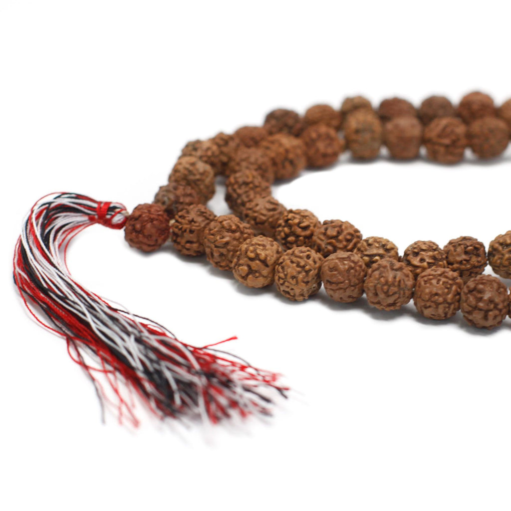 Gros plan sur des perles de rudraksha naturelles avec texture détaillée et pompon rouge et blanc attaché au mala.